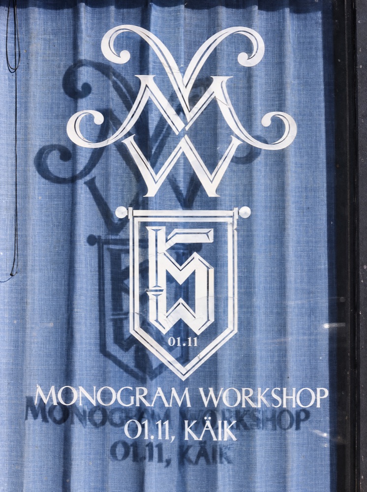 The MW monogram and a pennant with the words Monogram Workshop, 01.11, Käik on a window over a blue curtain